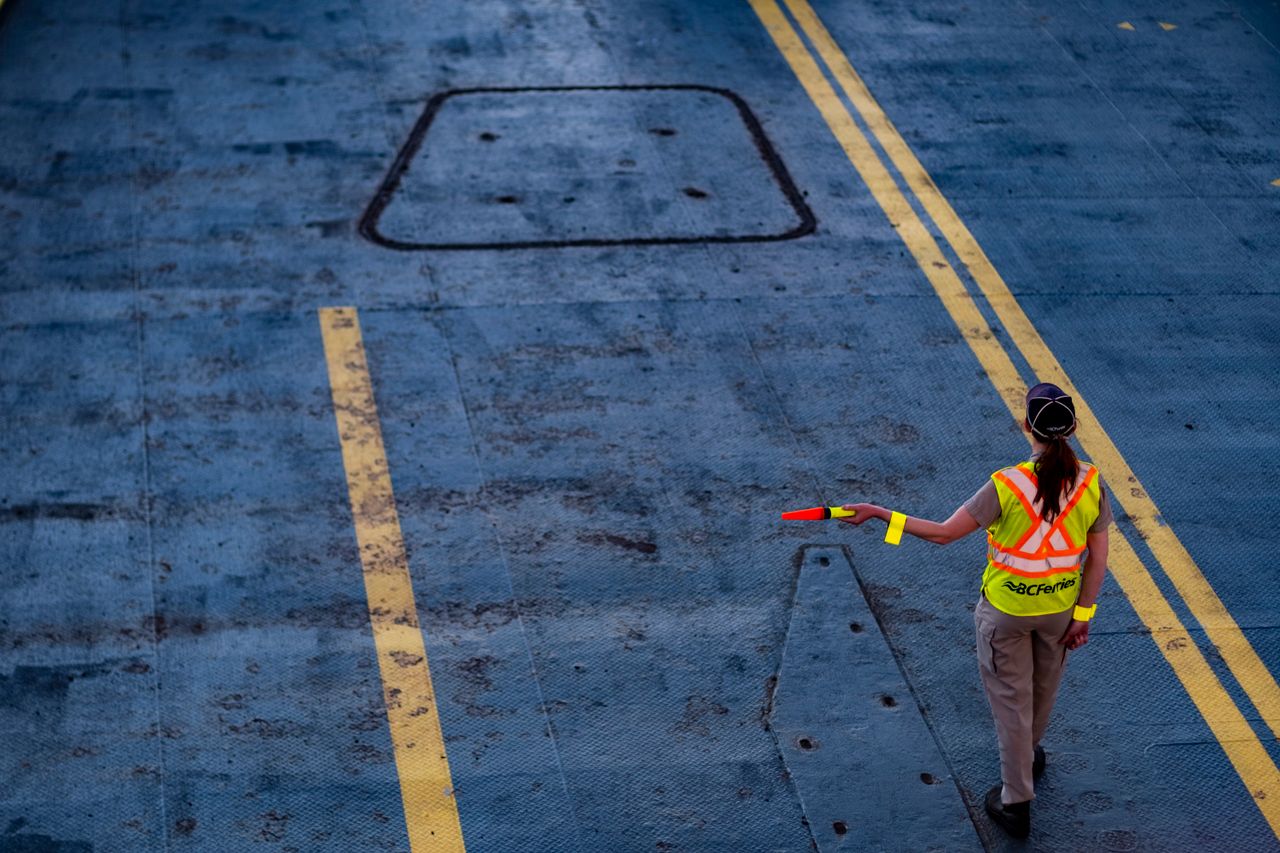 A BC Ferries worker directs traffic on the ferry deck, wearing a high-visibility jacket.