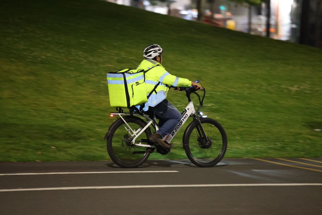 A delivery cyclist rides through the city at night with a reflective jacket and backpack.
